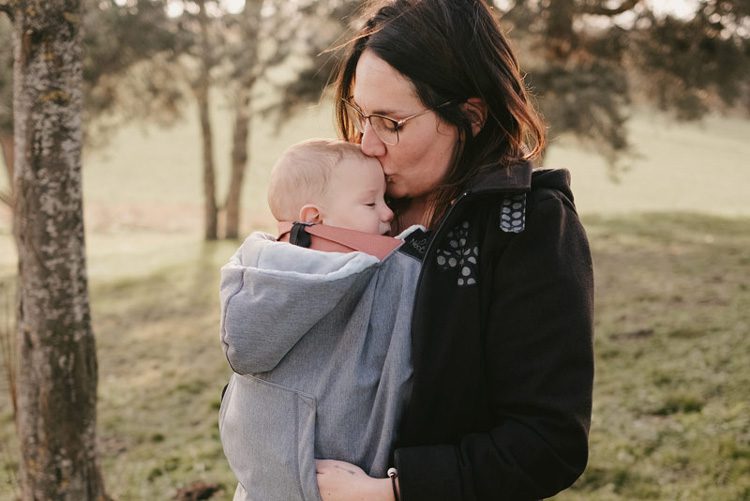 une maman porte son bébé, il est couvert avec une couverture de portage