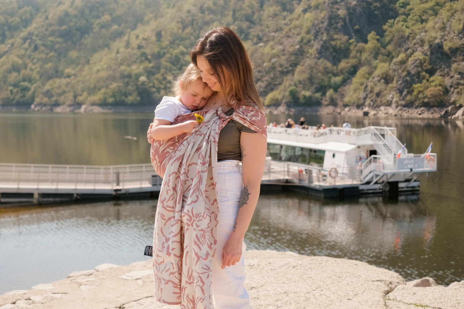 Porte bébé en voyage: photo d'une maman au bord d'un port, avec sa fille de 2 ans en sling Néobulle
