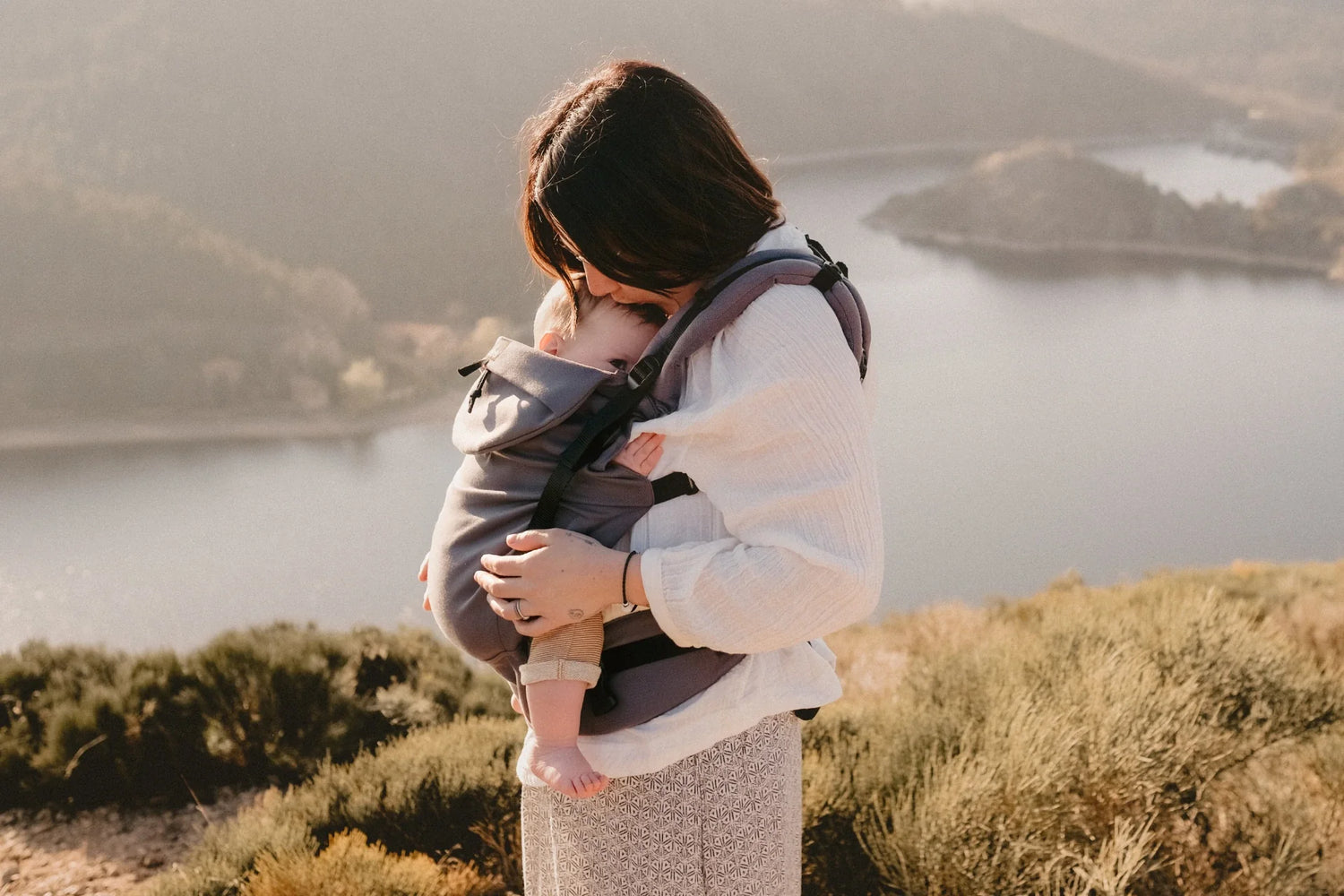 Bébé porté en porte-bébé l'été au bord d’un lac par sa mère, en Néo+.