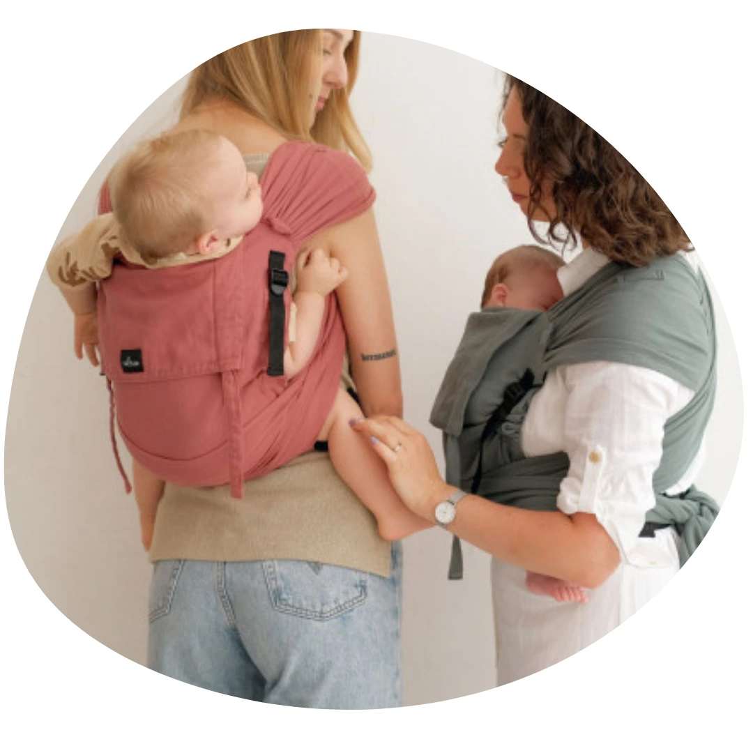 Echarpe de portage ou porte bébé : et si vous optiez pour une solution hybride ? Photo de deux mamans qui portent leurs enfants en Pti-Evo de Néobulle, la première en ventral, l'autre en dorsal.